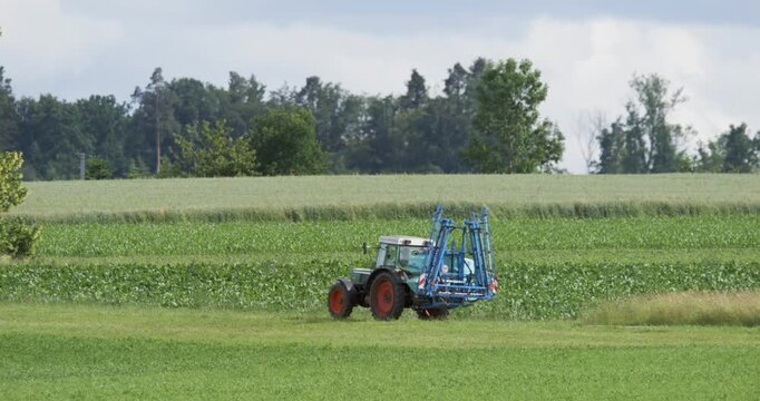 Tractor spraying a green crop field beside a tree line