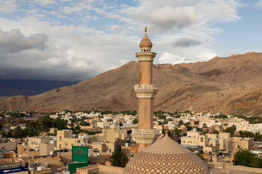 Nizwa city skyline with mosque minaret and mountains under dramatic sky, showcasing traditional Omani architecture and cultural tourism. Nizwa, Oman - April 6 2026