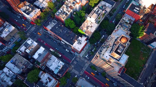 Aerial view of New York City street intersection. Birds eye view of Manhattan street crosswalk with yellow taxis, red bus lane, rooftops and trees.