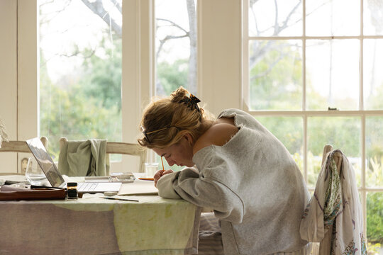 young woman artist using laptop as reference as she does a drawing in her studio