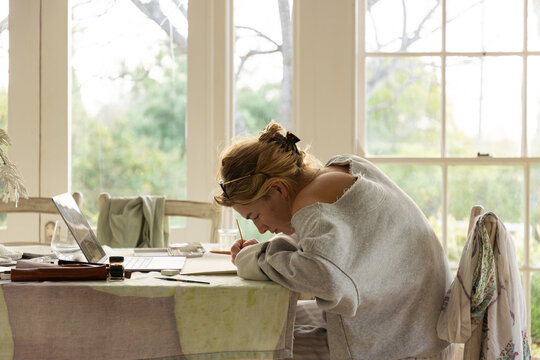 young woman artist using laptop as reference as she does a drawing in her studio