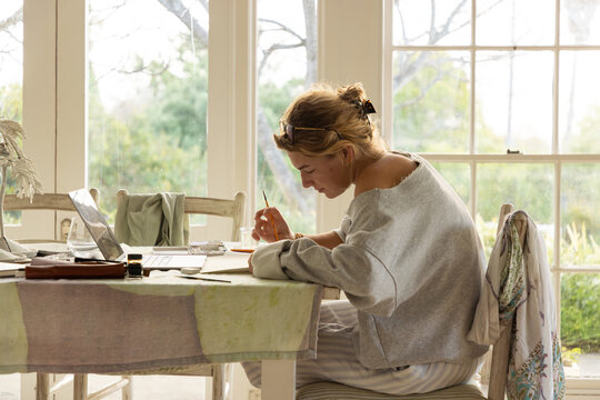 young woman artist using laptop as reference as she does a drawing in her studio