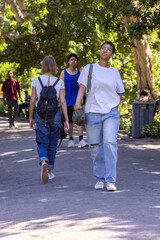 Obraz premium African American woman walking toward camera on park walkway carrying green shoulder bag