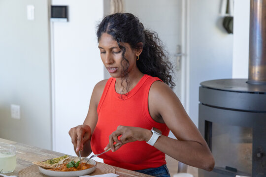 Asian woman in red top sitting at dining table cutting meal with fork and knife today