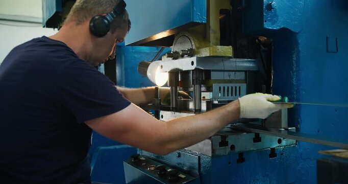 Blue collar machine operator handling metal parts at industrial press. Manufacturing work and factory workflow