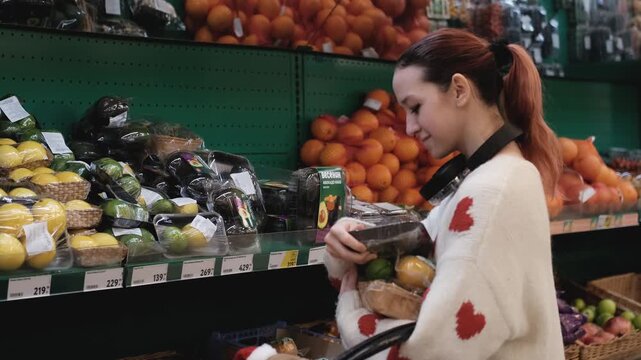 A young woman in a white wool sweater buys fruits at a supermarket in winter.