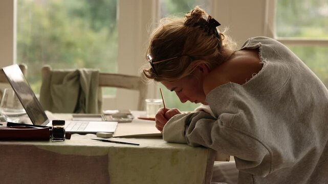 young woman artist using laptop as reference as she does a drawing in her studio