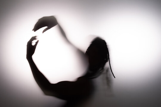 Anonymous Black American man dancing behind frost glass in studio with white background. 