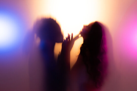 Couple cuddling and touching each other behind frost glass in warm light