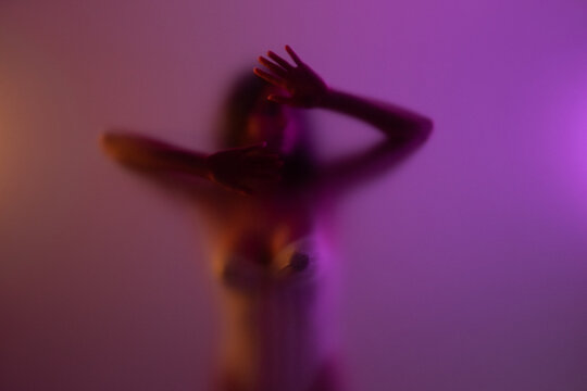 Woman posing behind frosted glass against purple background