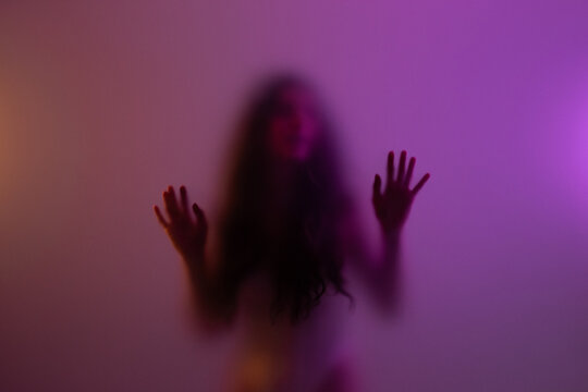 Anonymous young woman touching frosted glass in studio