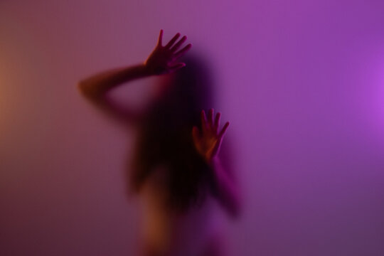Woman touching frost glass in purple light. Conceal, isolation and confinement concept