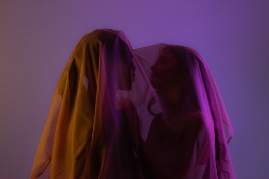 Young multiracial couple under transparent veil in studio. Discrete privacy concept. 