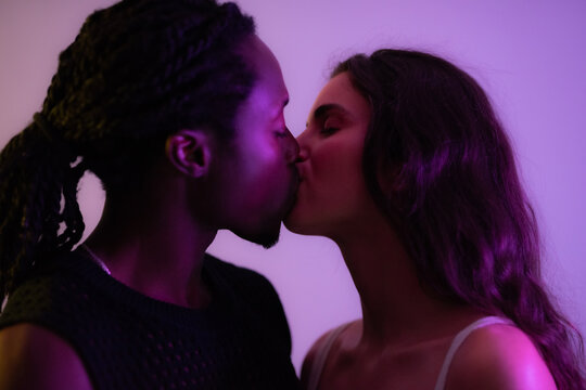 Multiracial young couple kissing. Studio shot against lilac background