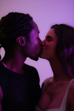 Happy multiracial young couple kissing with eyes closed at studio with purple background. Closeup portrait. 