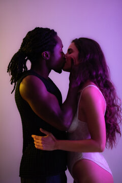 Passionate and loving multiracial young couple kissing against purple background at studio 