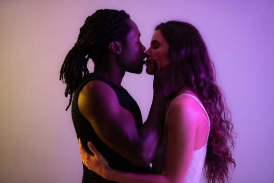 Loving multiracial couple kissing at studio against purple background. They show tenderness and desire