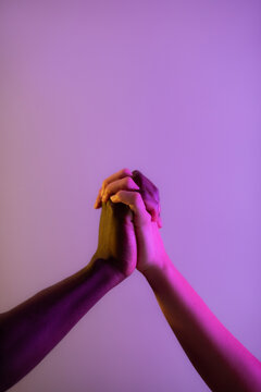 Anonymous multiracial couple holding hand firmly at studio with lilac background 