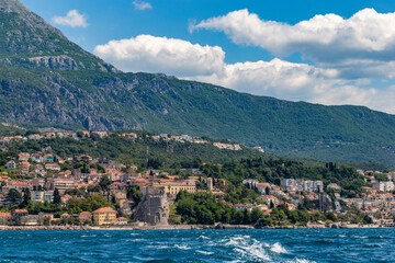 Fototapeta premium Imposing medieval stone fortress rising majestically above the sunlit harbor and marina of Herceg Novi