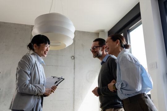 Real estate agent meeting with a multicultural couple during a property consultation. Professional discussion about buying, renting, or investing in a new home