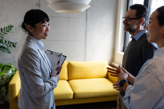Real estate professional guiding a multicultural couple through a new apartment, discussing relocation, housing options, and investment opportunities in a modern property