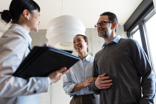 Professional real estate advisor explaining housing options to a mature multicultural couple. Concept of renting, investing, relocation, and property planning