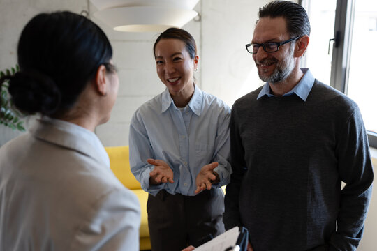 Happy diverse couple laughing with a real estate agent during an apartment tour. Smiling multicultural clients looking at paperwork, discussing a property lease, home purchase, or mortgage deal