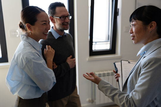 Happy diverse couple on an apartment tour with their real estate agent. Smiling multicultural buyers talking to a realtor, exploring a new property, home, or commercial space to rent or buy.