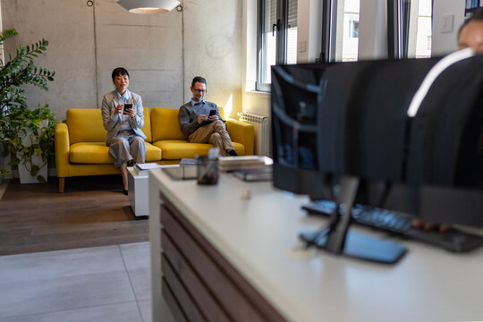 Business professionals waiting in office reception area before meeting. Mobile technology, workplace routine and modern corporate environment concept