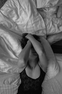 Artistic black and white overhead view of a sensual woman in black lace lingerie lying on white bed sheets, covering her face. Moody bedroom atmosphere and morning light, low key, selective focus, bac