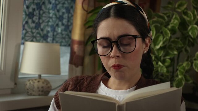 Portrait of Caucasian female showing dissatisfaction with a book while sitting comfortably indoors. Reading and critical opinion concept