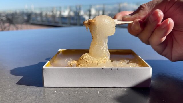きな粉をトッピングした和菓子のわらび餅の動画。木製スプーンで食べようとしてる様子。