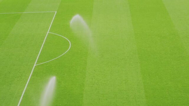Automated sprinklers hydrating a bright green soccer pitch, maintaining optimal playing surface conditions for sports