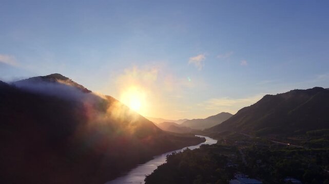 Aerial drone view of sunrise over a mountain valley with winding river and morning mist in northern Vietnam. Cinematic landscape with golden light and dramatic scenery.