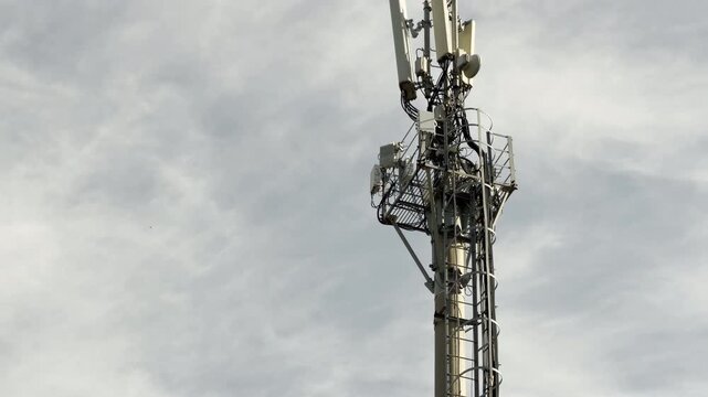 A metal communication tower stands tall against a grey, cloudy sky. Its complex array of antennas evokes a feeling of lonely industrial precision and modern connectivity.