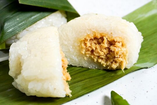 Close up sliced in half lemper ayam Indonesian sticky rice with chicken filling snack isolated on horizontal banana leaf and white plate background.