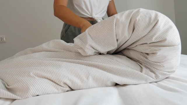 Hands folding striped duvet on white bed, minimalist bedroom interior, daily home routine and housework, commercial lifestyle use.
