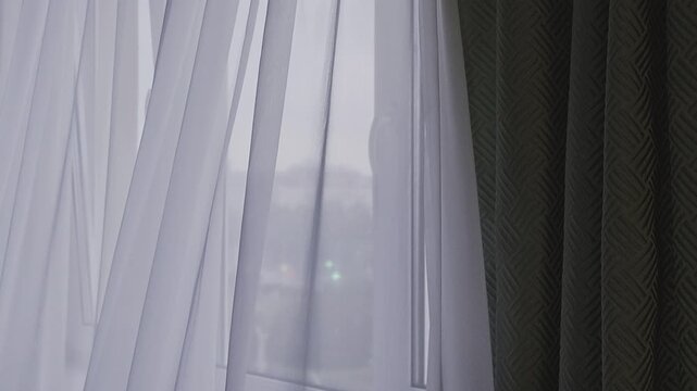The soft white sheer curtains gently filter the sunlight pouring in through the window, casting a calm ambiance that complements the rich, intricately patterned green drapes