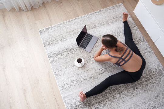 sporty young woman sit on floor in living room practice yoga on online computer lesson. female meditate train at home watching having class on webcam on laptop