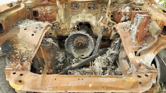 A completely burned and rusted car chassis rests ruined outdoors. This empty, gutted engine bay evokes a deep sense of sadness, eerie despair, and heartbreak.