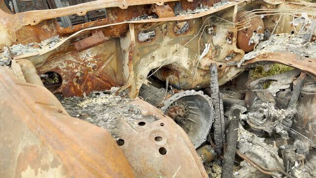 A completely burned and rusted car chassis lies destroyed outdoors. This charred engine compartment evokes a deep sense of sadness, grim despair, and heartbreaking ruin.