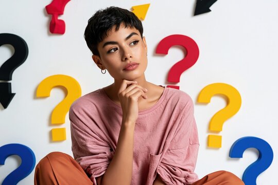 Young seated woman thinking against colorful question mark wall pattern for idea concept background poster and banner design