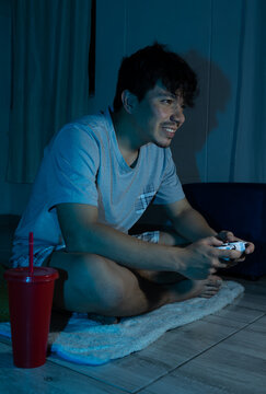 Young man sitting on the living room floor enjoying a video game session at night. Digital entertainment, fun, leisure, and modern lifestyle concept