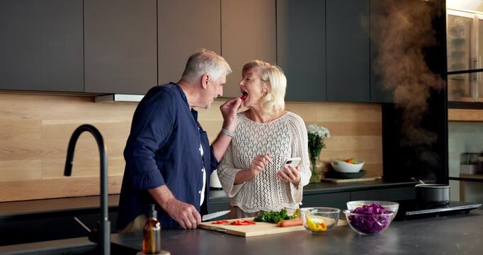 Couple, reading and phone in home for cooking, recipe and online tutorial for healthy food. Mature people, feeding and laugh at house with mobile, instructions and meal prep with vegetables for lunch