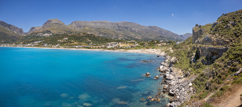 Panoramic image of beach and bay of Plakias, Crete, Greece. Unidentifiable sunbathers, parasols and sunbeds on the beach.