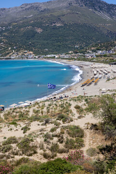 The beach and bay of Plakias, Crete, Greece. Unidentifiable sunbathers, parasols and sunbeds on the beach.