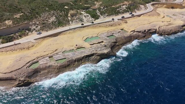 At Xwejni in Zebbug on Gozo, the traditional Maltese salt pans form geometric pools along the rocky Mediterranean coastline, captured in a drone view that shows their limestone layout.