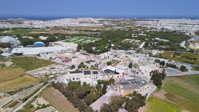 In Ta' Qali, Malta, Park Nazzjonali is shown with its green spaces, walking paths, event venues and surrounding farmland and roads captured in a wide drone view.