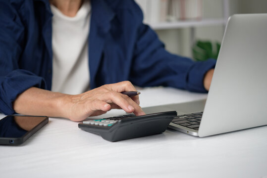 Senior person calculating finance budget using calculator laptop computer accounting tax retirement planning financial savings investment working home office desk banking concept