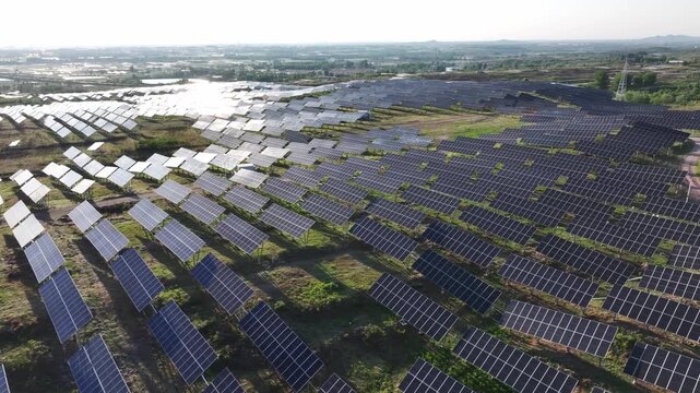 Aerial view of a large-scale photovoltaic power station with solar panels arranged in neat rows across rural fields and wetlands